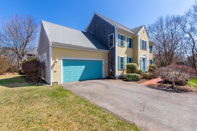 colonial house featuring an attached garage, roof with shingles, driveway, and a front yard