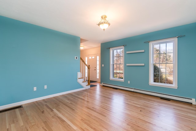 unfurnished room with wood finished floors, a baseboard heating unit, baseboards, and stairs