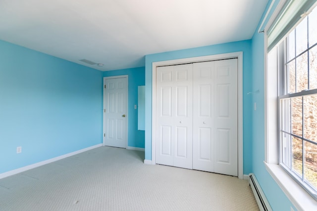 unfurnished bedroom featuring a closet, light colored carpet, a baseboard heating unit, and baseboards