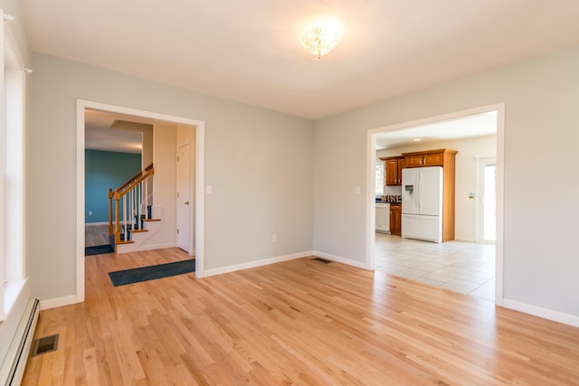 empty room featuring light wood-style flooring, a baseboard heating unit, baseboards, and stairs
