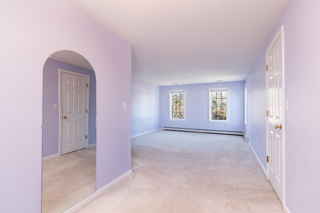 corridor with a baseboard radiator, baseboards, light carpet, and arched walkways