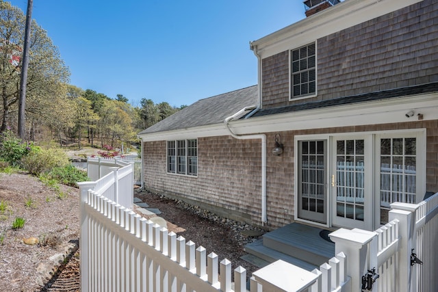 view of home's exterior featuring fence, a chimney, and roof with shingles