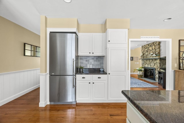 67 Sea Meadow Cir, Centerville, MA 02632 - kitchen with freestanding refrigerator, wood finished floors, dark stone countertops, white cabinetry, and a stone fireplace