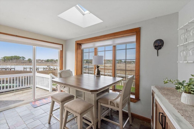 dining room featuring a skylight, a water view, stone finish floor, and a wealth of natural light