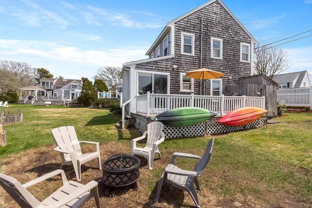rear view of property with a lawn, a deck, and a fire pit