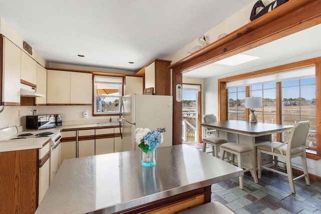 kitchen with stone finish floor, a sink, light countertops, under cabinet range hood, and white appliances