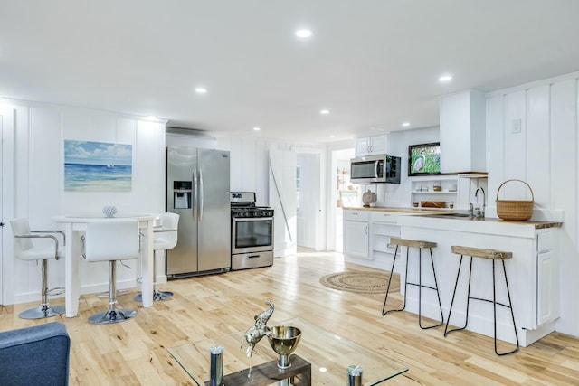 kitchen featuring white cabinetry, stainless steel appliances, a breakfast bar, and light wood-type flooring