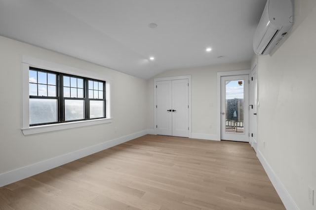 interior space with a wall mounted air conditioner, light hardwood / wood-style flooring, and vaulted ceiling