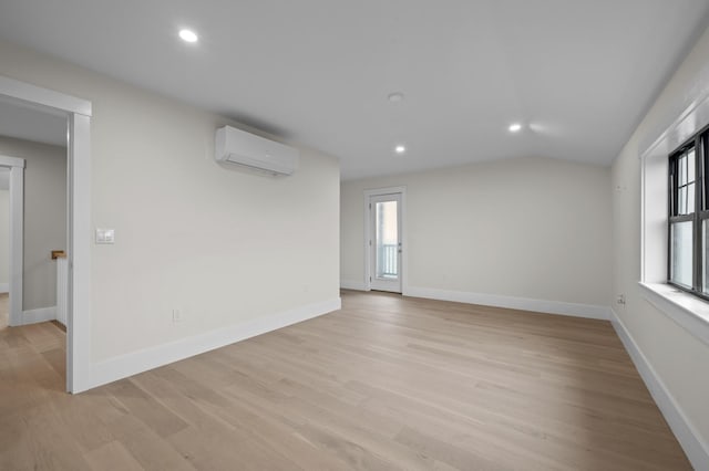 empty room with plenty of natural light, vaulted ceiling, a wall unit AC, and light wood-type flooring