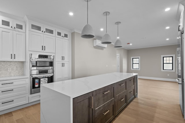 kitchen with appliances with stainless steel finishes, tasteful backsplash, white cabinetry, a kitchen island, and a wall unit AC