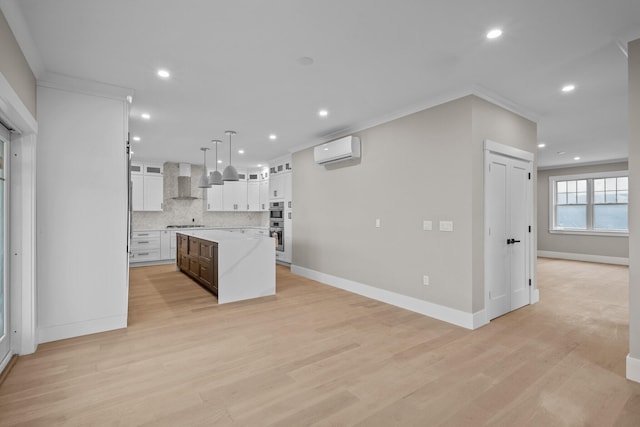 kitchen with crown molding, hanging light fixtures, white cabinets, a center island, and wall chimney range hood