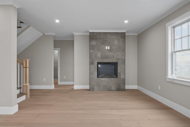 unfurnished living room featuring light wood-type flooring, ornamental molding, a tiled fireplace, and a healthy amount of sunlight