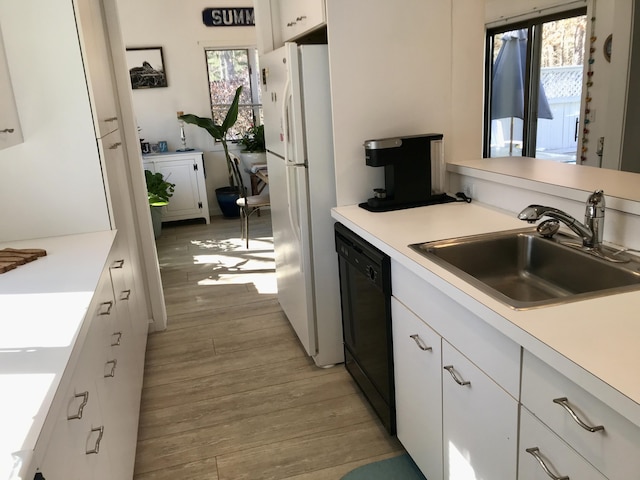 kitchen with light wood-style flooring, a sink, a healthy amount of sunlight, black dishwasher, and freestanding refrigerator