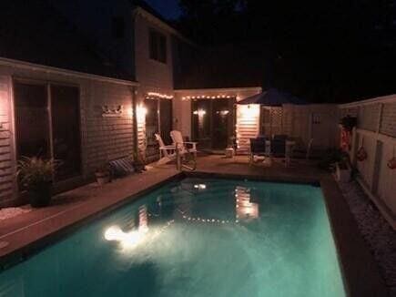 pool at night with a patio area, a fenced backyard, and an outdoor pool