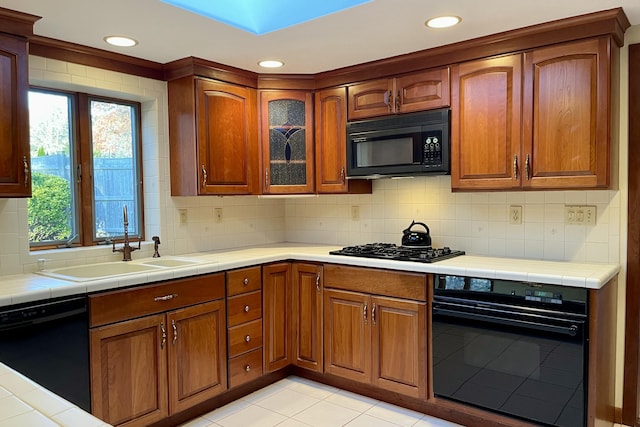 kitchen with black appliances, tile counters, light tile patterned floors, decorative backsplash, and sink