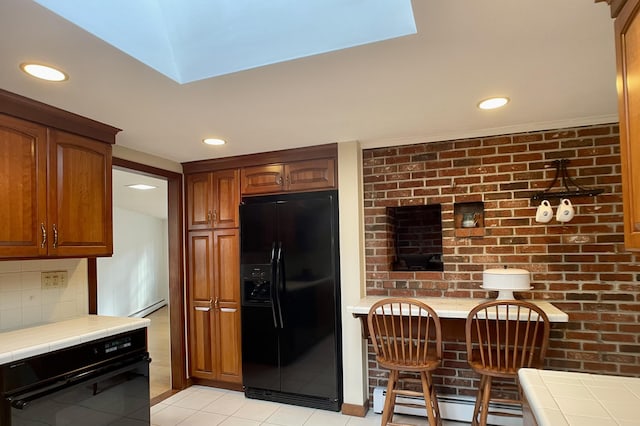 kitchen with a baseboard radiator, light tile patterned floors, black appliances, decorative backsplash, and tile counters