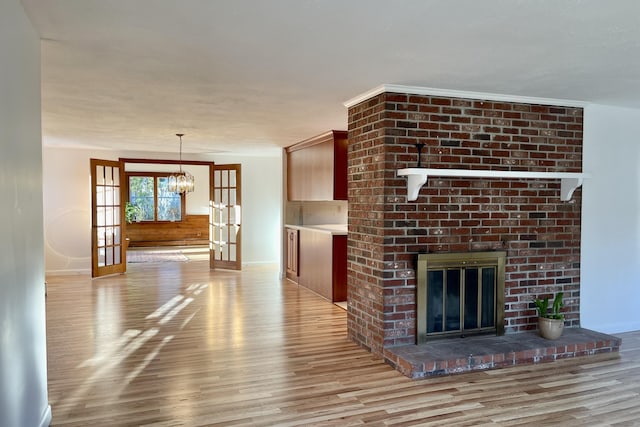 unfurnished living room with french doors, a fireplace, ornamental molding, a notable chandelier, and light wood-type flooring