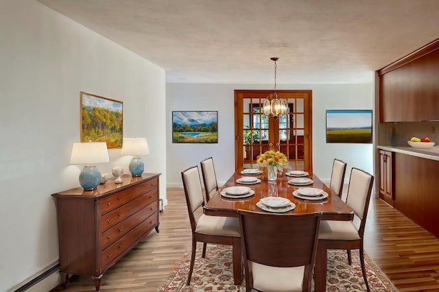 dining space featuring baseboard heating, light wood-type flooring, and an inviting chandelier