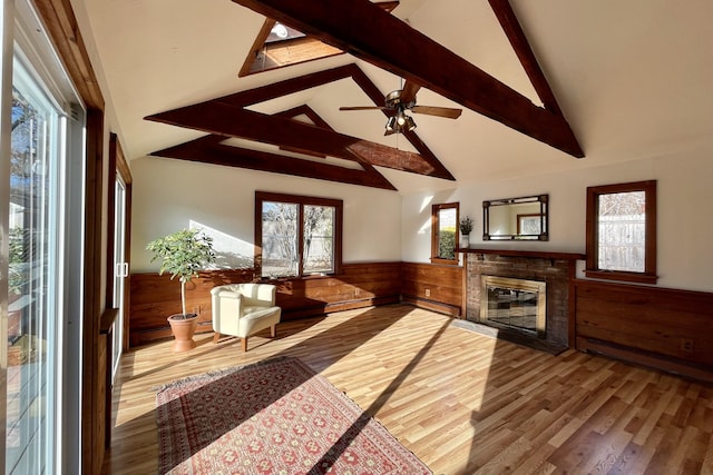 living room with wooden walls, ceiling fan, hardwood / wood-style flooring, lofted ceiling with beams, and a brick fireplace