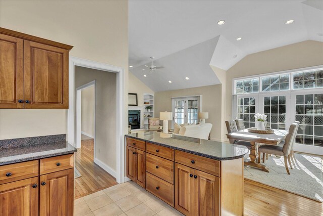 kitchen featuring ceiling fan, light tile patterned floors, lofted ceiling, and dark stone counters