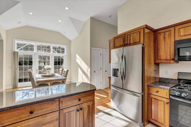 kitchen featuring black appliances, vaulted ceiling, dark stone countertops, and light tile patterned flooring