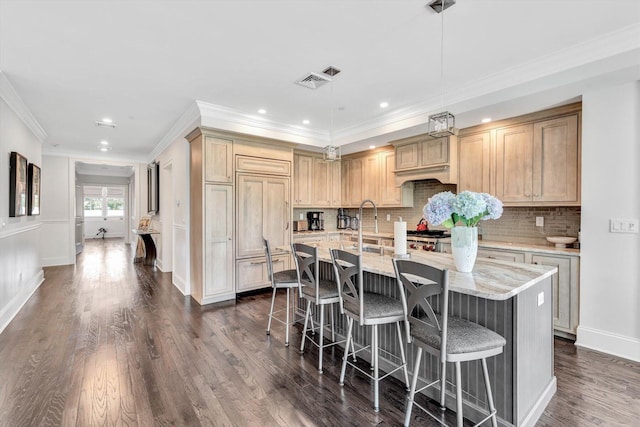 kitchen featuring dark wood-style flooring, visible vents, backsplash, an island with sink, and a kitchen bar