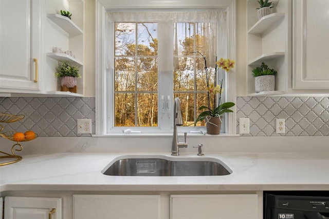 kitchen with white cabinetry, black dishwasher, sink, and light stone counters