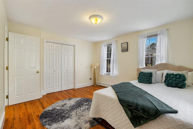 bedroom with wood-type flooring, a baseboard heating unit, and a closet