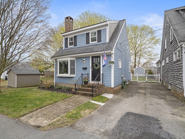 17 Edwards Rd, Hyannis, MA 02601 - view of front of property featuring an outdoor structure, a front lawn, a chimney, a shingled roof, and a storage shed
