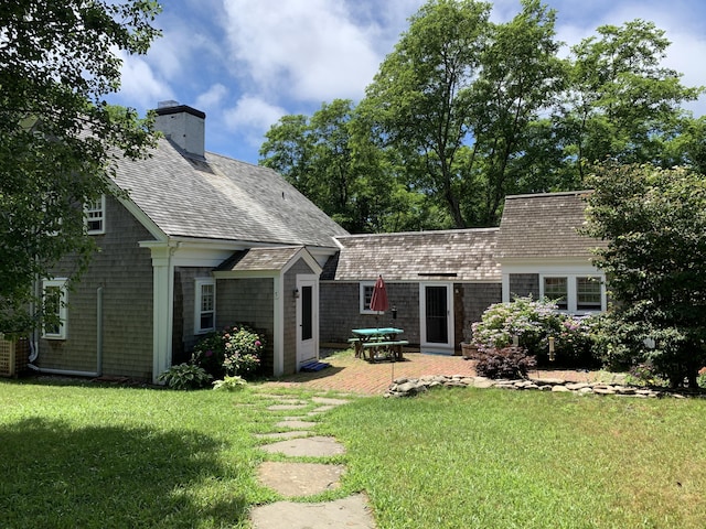 rear view of property featuring a shingled roof, a patio area, a yard, and a chimney