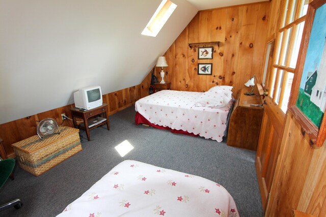 carpeted bedroom featuring vaulted ceiling with skylight and wooden walls