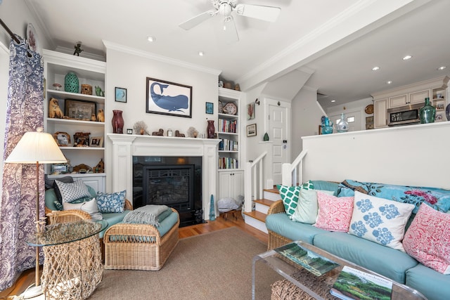 living area featuring a ceiling fan, built in features, wood finished floors, ornamental molding, and stairs