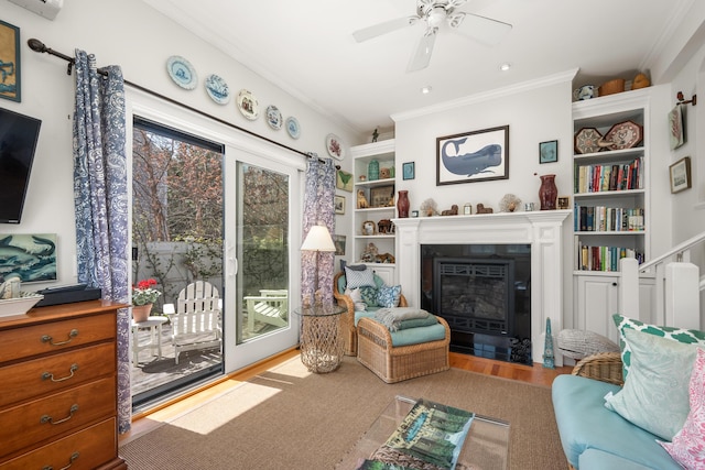 living room featuring crown molding, ceiling fan, built in shelves, a fireplace with flush hearth, and wood finished floors