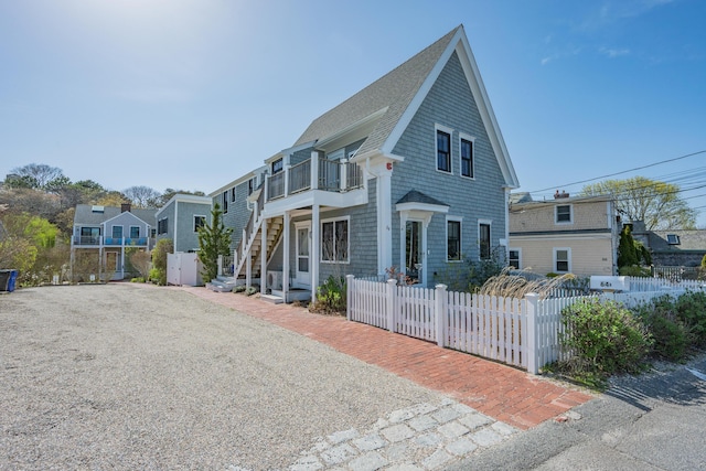 view of front of property with a balcony, stairs, a shingled roof, a fenced front yard, and a residential view