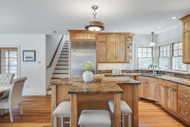 kitchen featuring a sink, built in refrigerator, a center island, light wood finished floors, and a kitchen bar