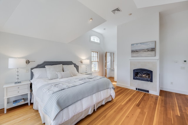 bedroom featuring a fireplace, baseboards, light wood-type flooring, and high vaulted ceiling