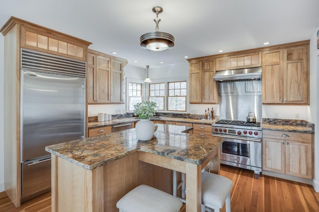 kitchen featuring high end appliances, range hood, a breakfast bar area, light wood-style floors, and recessed lighting