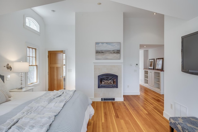 bedroom featuring high vaulted ceiling, a fireplace, wood finished floors, and baseboards