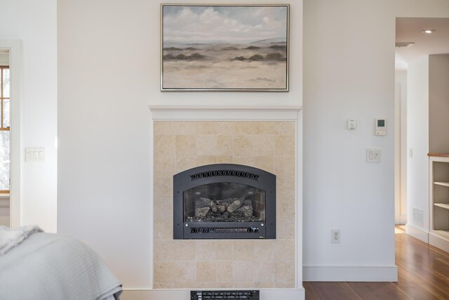 detailed view of a tile fireplace, wood finished floors, and baseboards