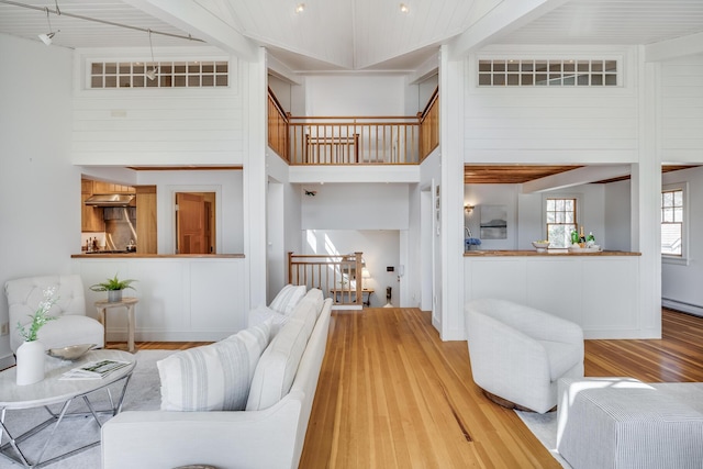 living area featuring wood finished floors, a towering ceiling, and a baseboard radiator