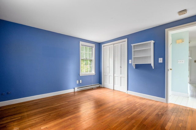 unfurnished bedroom with a closet, hardwood / wood-style flooring, and a baseboard heating unit