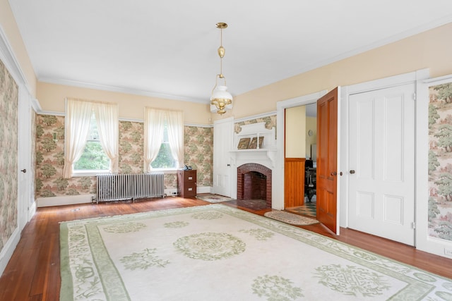 unfurnished living room with radiator heating unit, a brick fireplace, crown molding, and wood-type flooring