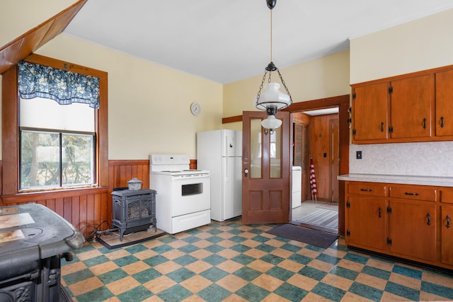 kitchen with washer / dryer, decorative light fixtures, a wood stove, white appliances, and wood walls