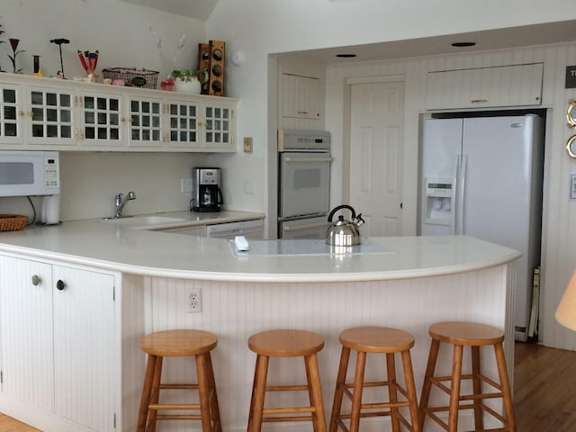 kitchen with white appliances, light hardwood / wood-style floors, sink, kitchen peninsula, and a breakfast bar area