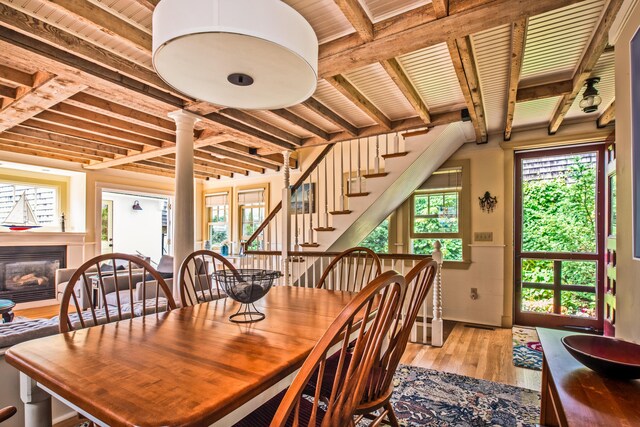 351A Commercial St Unit A1, Provincetown, MA 02657 - dining area featuring light wood-type flooring, stairs, a glass covered fireplace, a wooden ceiling with exposed beams, and decorative columns