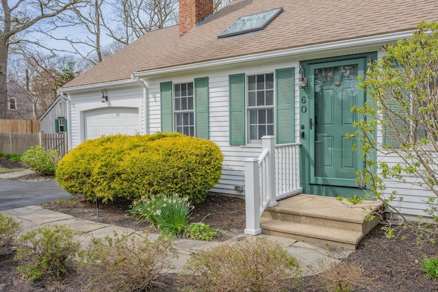 60 Covey Dr, Yarmouth Port, MA 02675 - view of exterior entry with an attached garage, roof with shingles, fence, and a chimney