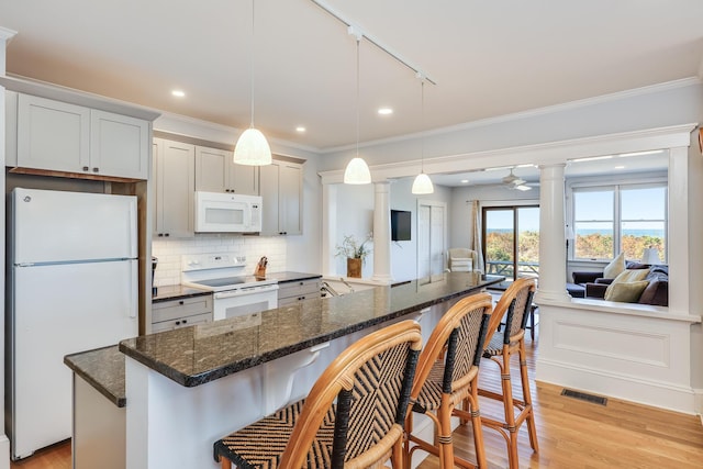 kitchen with white appliances, ornate columns, track lighting, pendant lighting, and a breakfast bar area