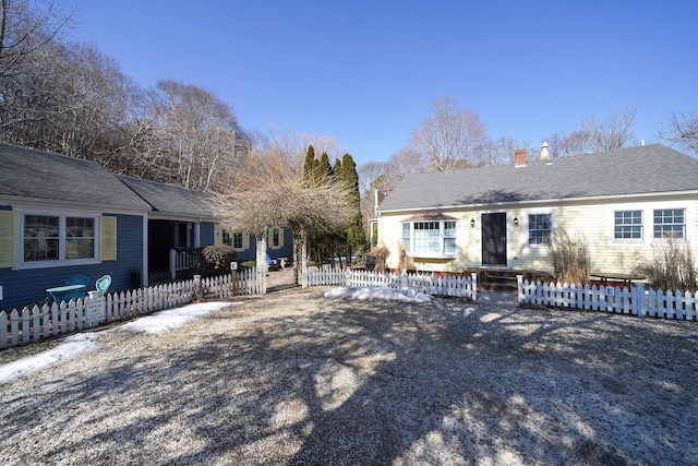 ranch-style home featuring entry steps, a fenced front yard, and roof with shingles