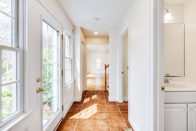 hallway with a sink, baseboards, light tile patterned flooring, and a wealth of natural light