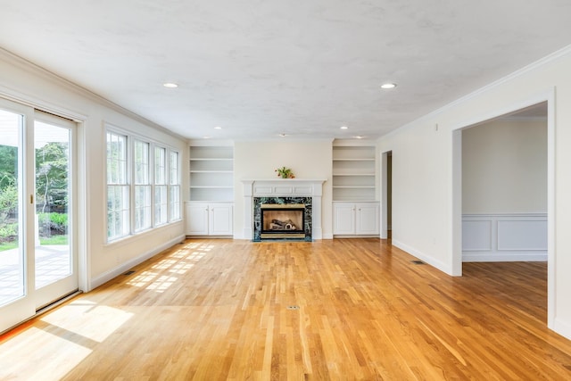 unfurnished living room with light wood-style floors, a premium fireplace, built in shelves, recessed lighting, and ornamental molding